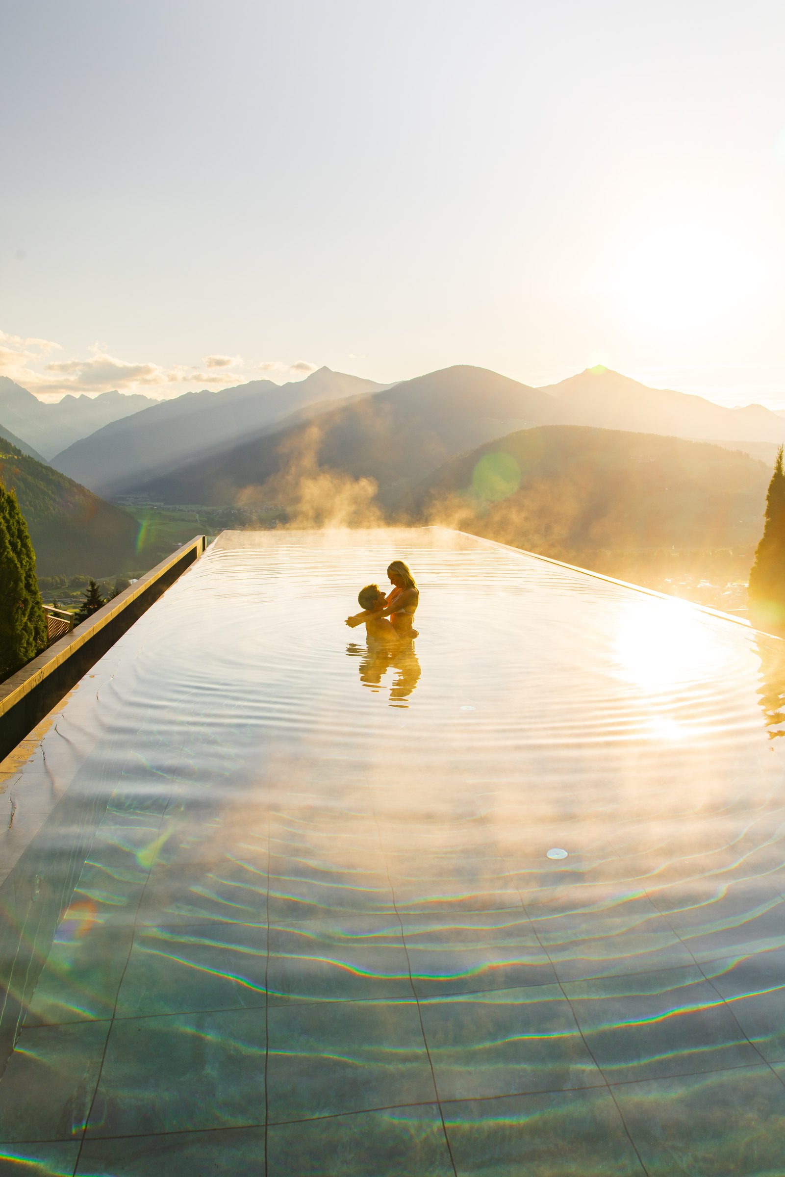Swimmer in the steaming infinity sky pool at Hotel Hubertus as the sun rises over the mountains
