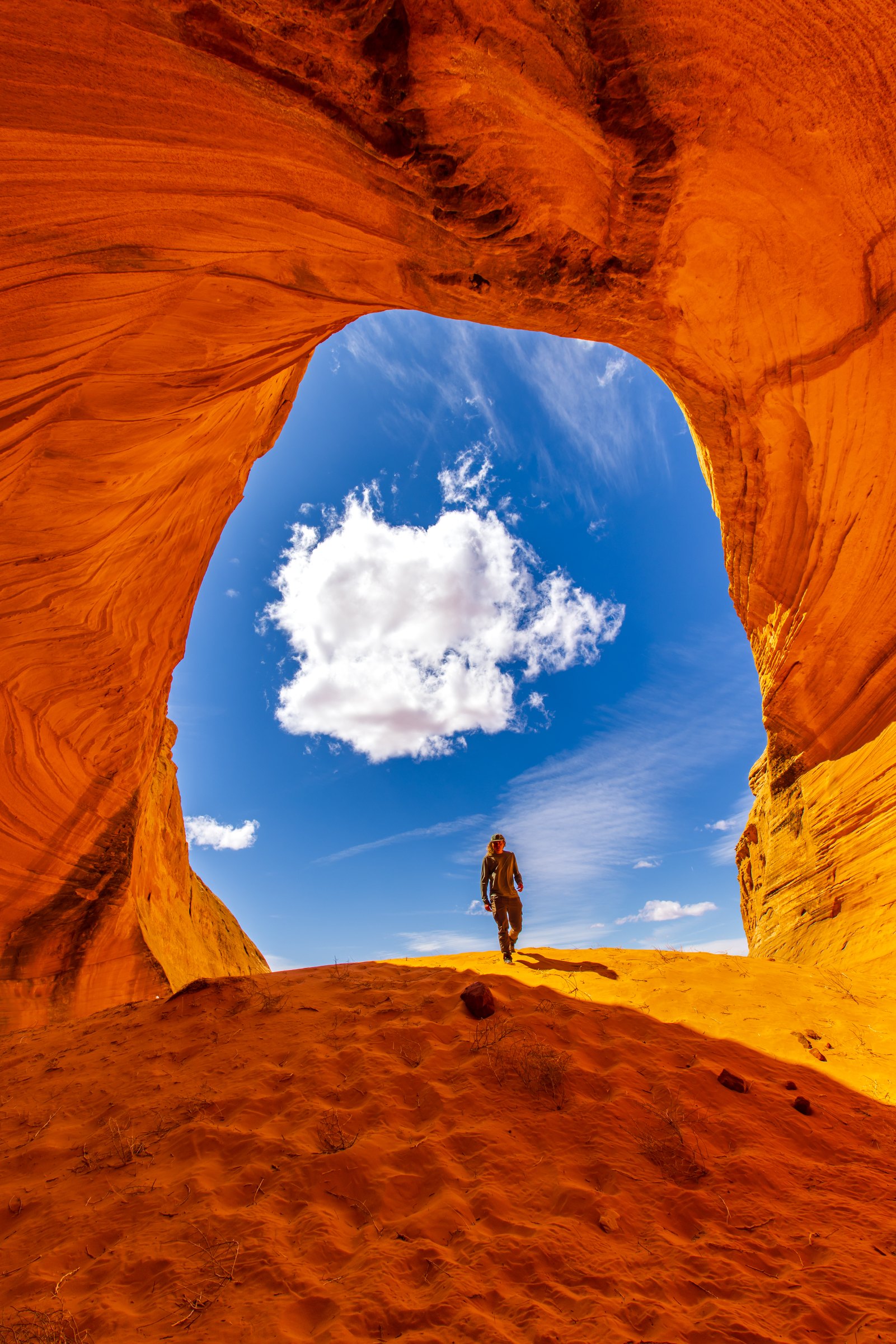 Hiker beneath a red sandstone arch with a single cloud in the opening