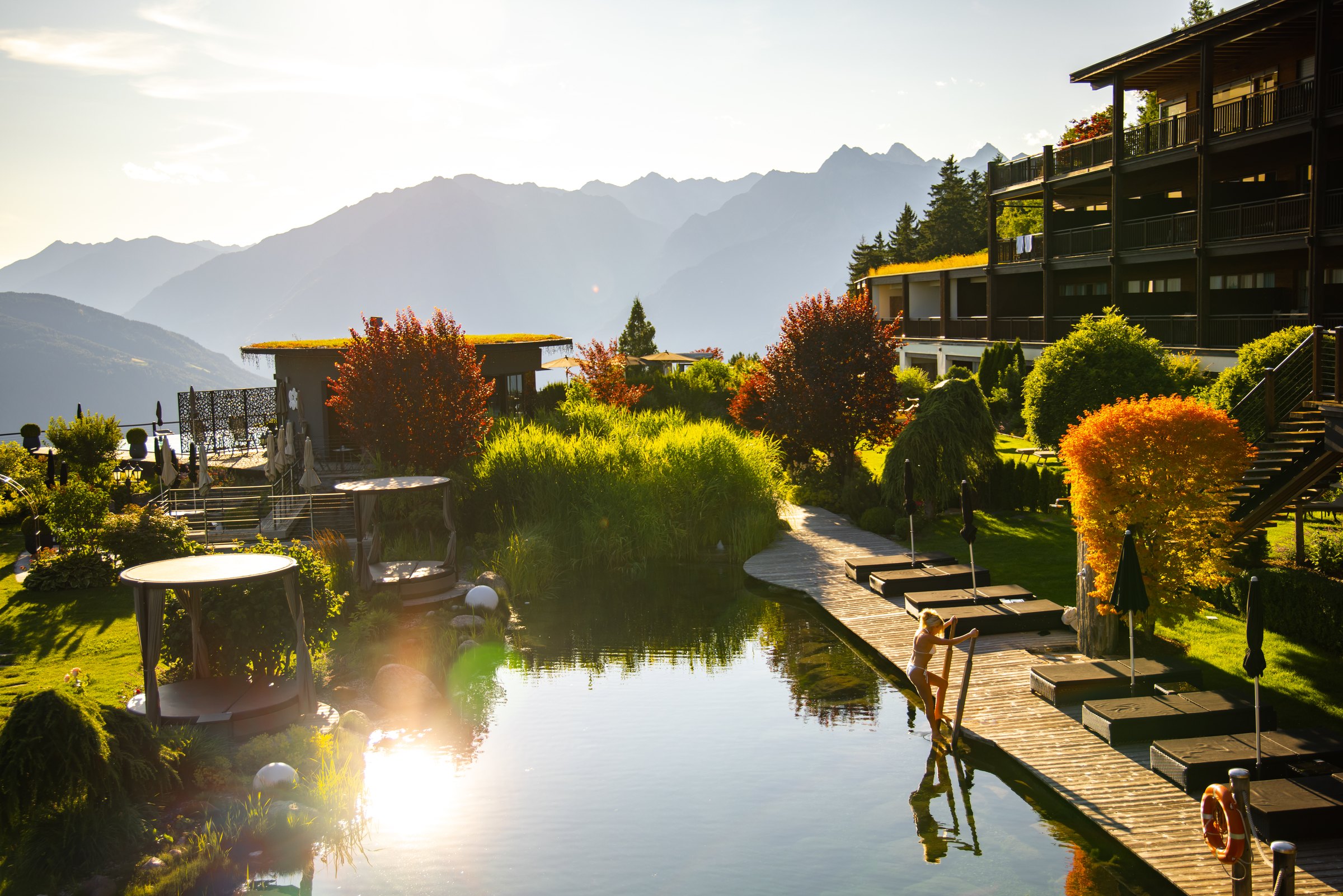 Natural bio pool and gardens at Chalet Mirabell glowing in the late sun with mountains beyond