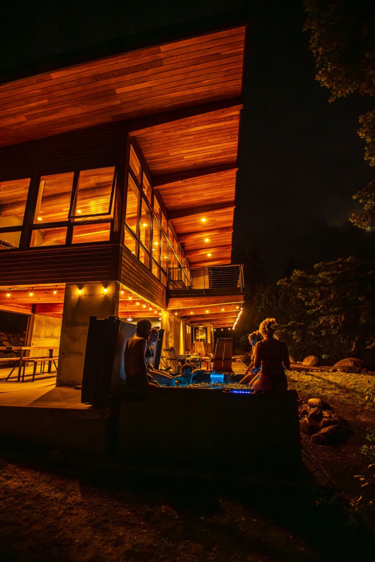 Hot tub glowing at night beneath the modern timber vacation home at Wander Leavenworth River