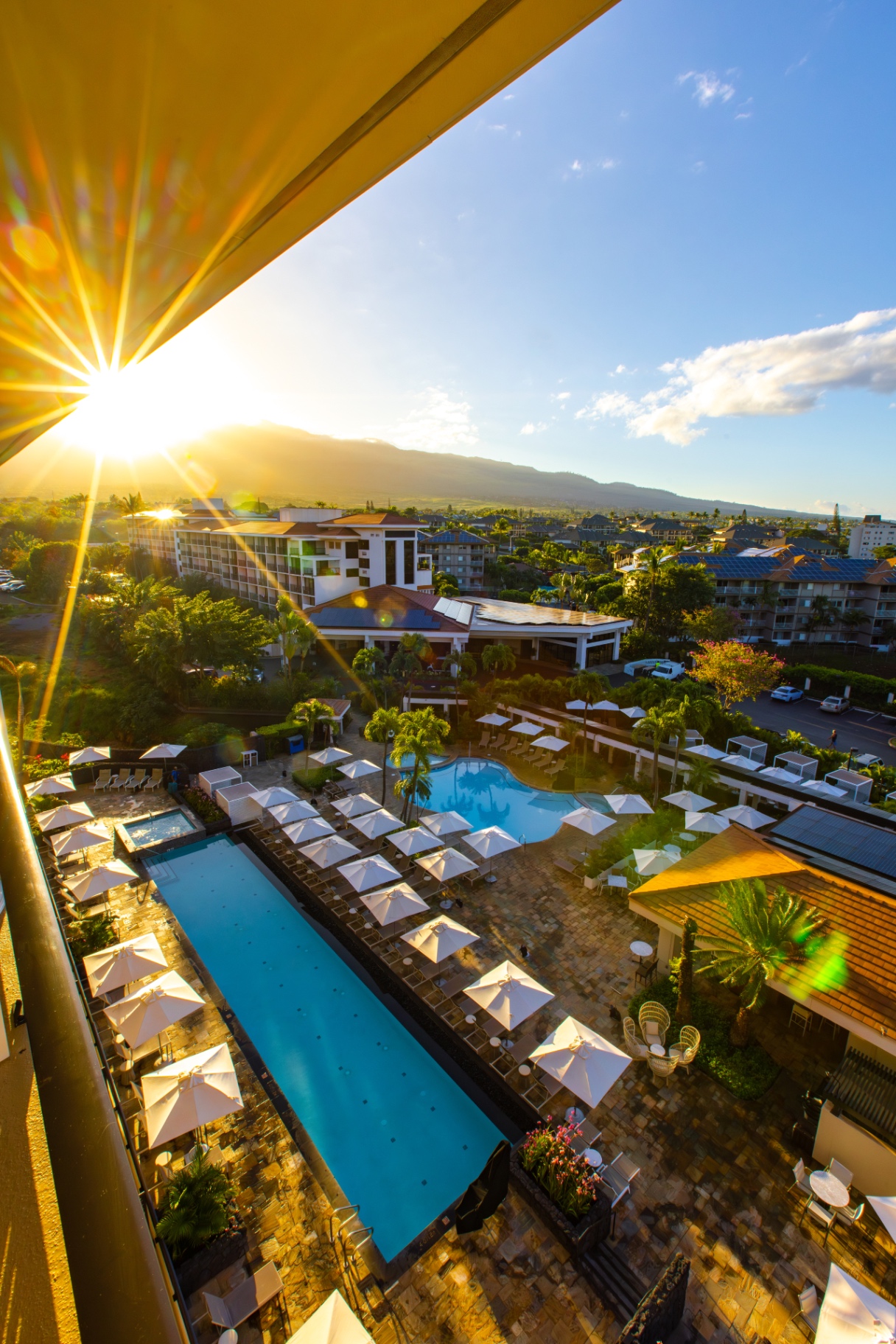 Sunlit pool deck with white umbrellas at Maui Coast Hotel seen from a balcony