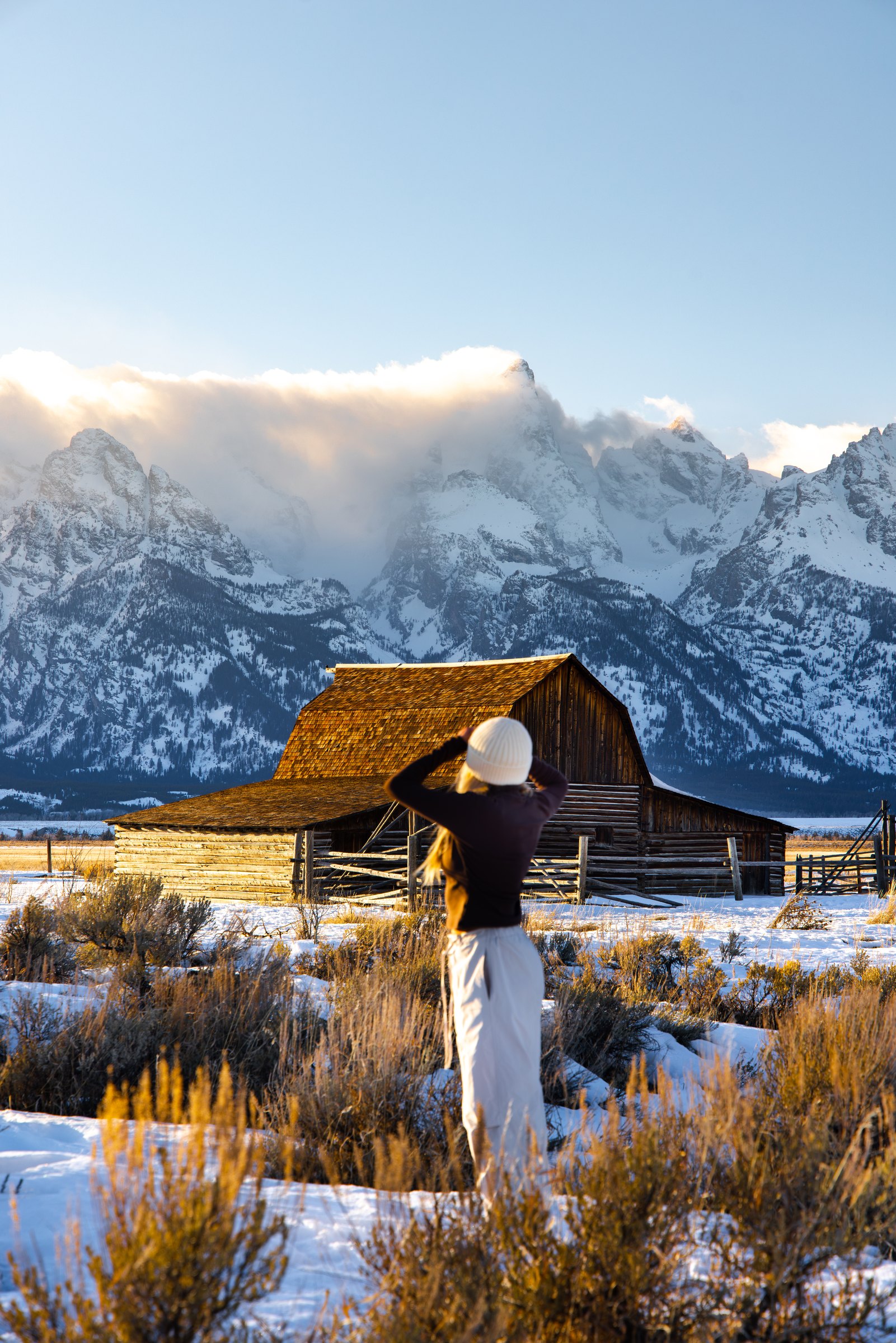 Woman photographing a historic barn below the snowy Teton Range