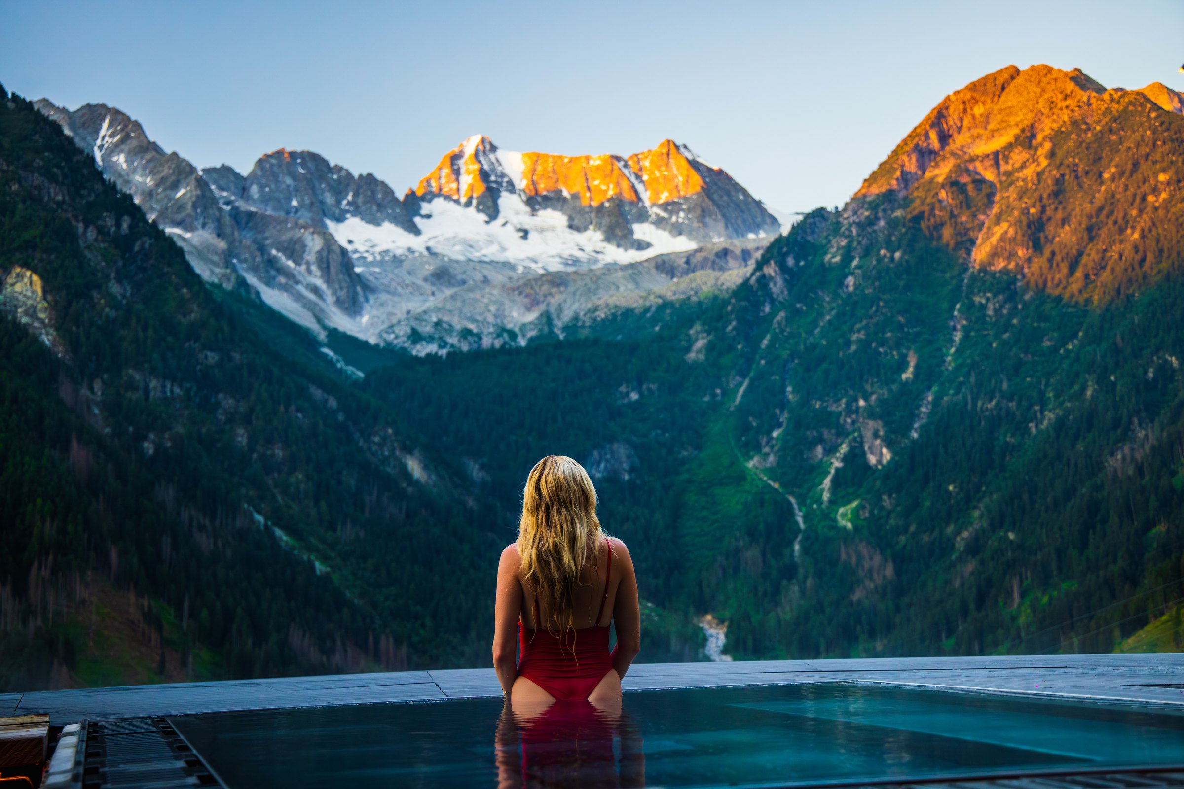 Guest in the infinity pool at Chalet Al Foss facing jagged peaks lit by morning sun