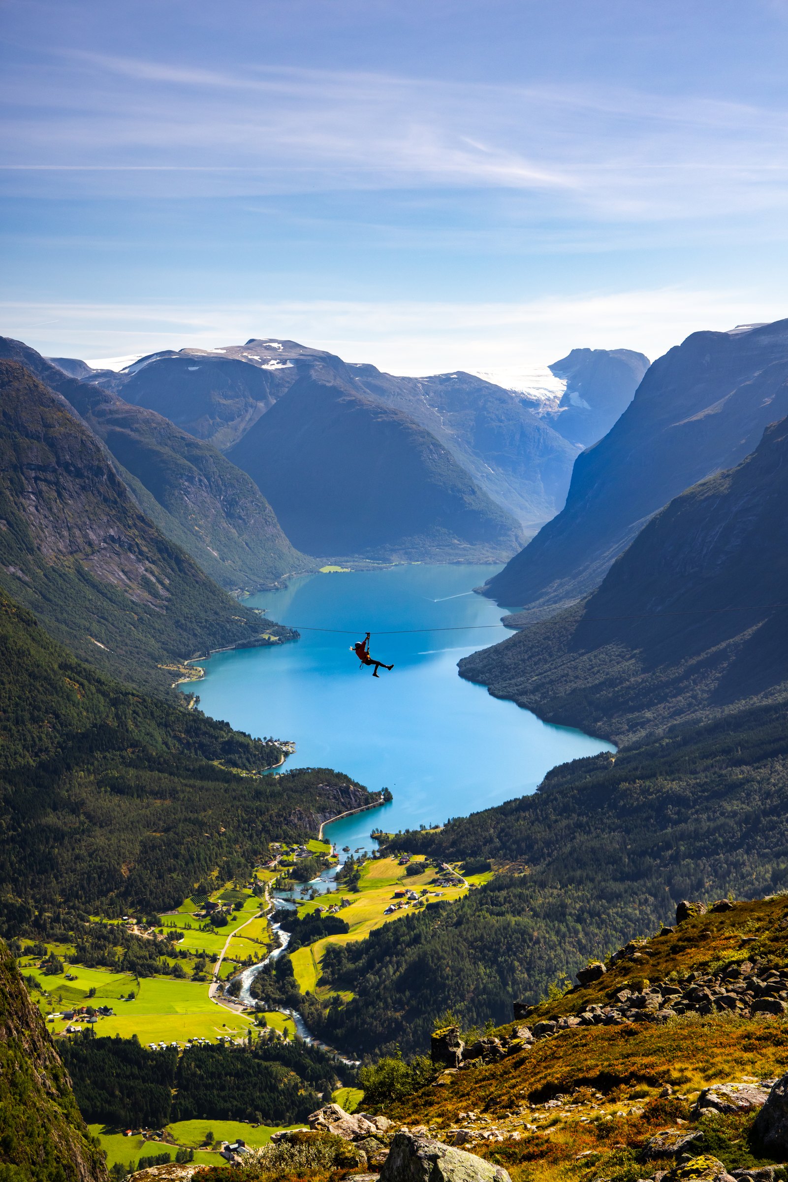 Person on a zipline high above a green valley and turquoise fjord near Loen, Norway