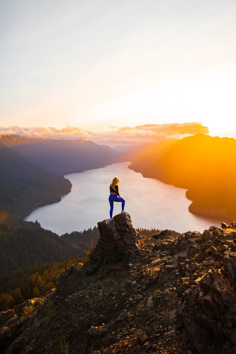 Hiker standing on a rocky summit above Lake Crescent at golden sunset, Mount Storm King