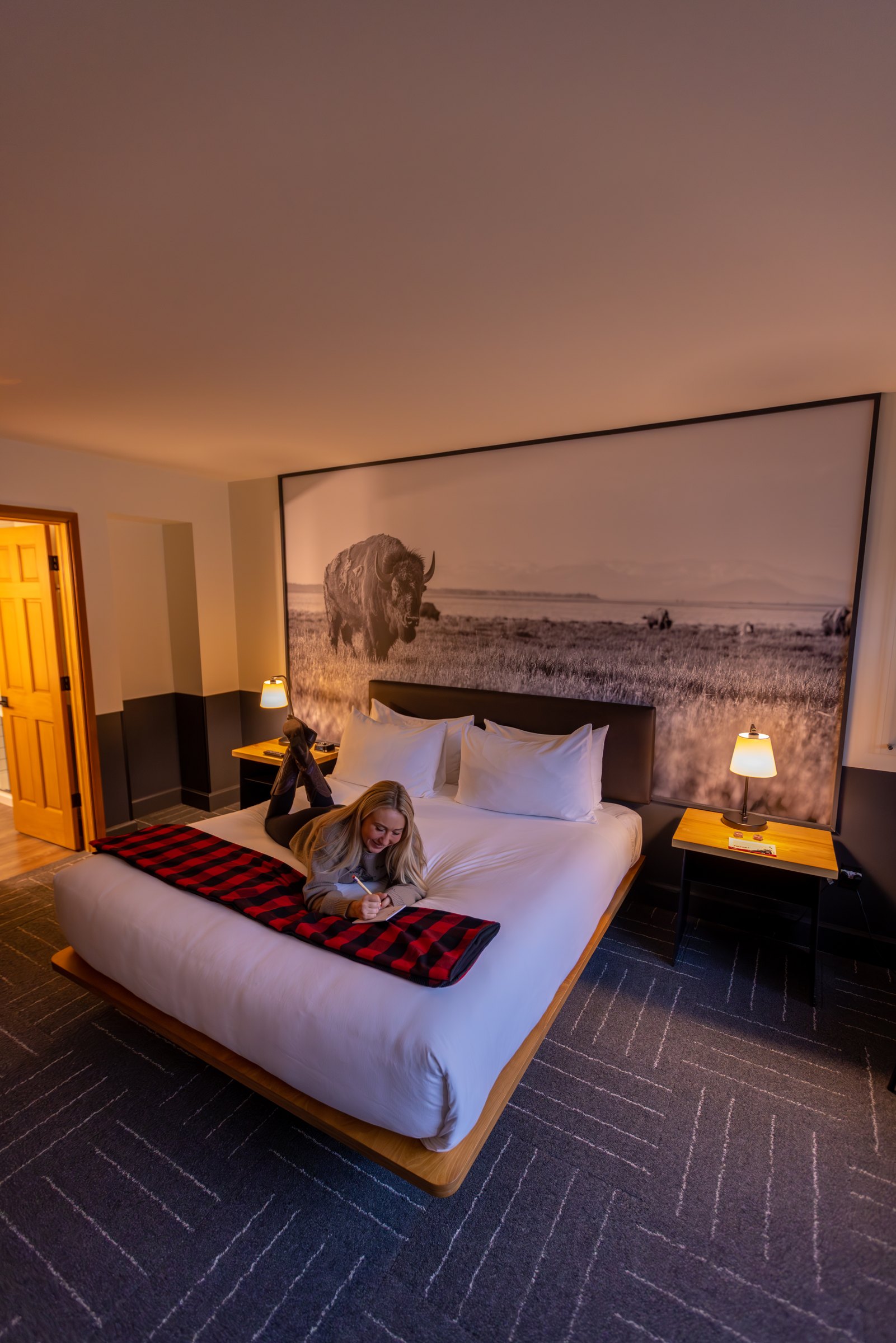 Guest relaxing on a bed below a large black and white bison mural at Mountain Modern Motel