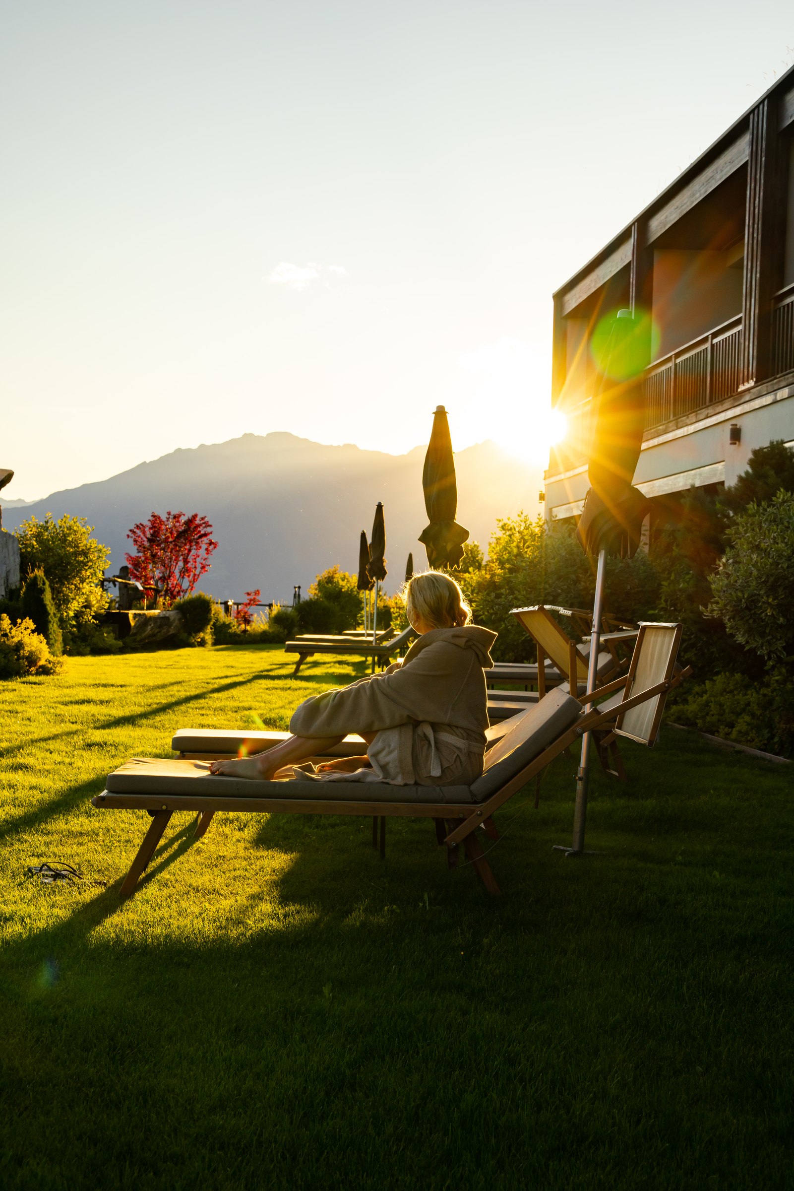 Guest on a lounger on the lawn at Chalet Mirabell as the sun sets behind the mountains