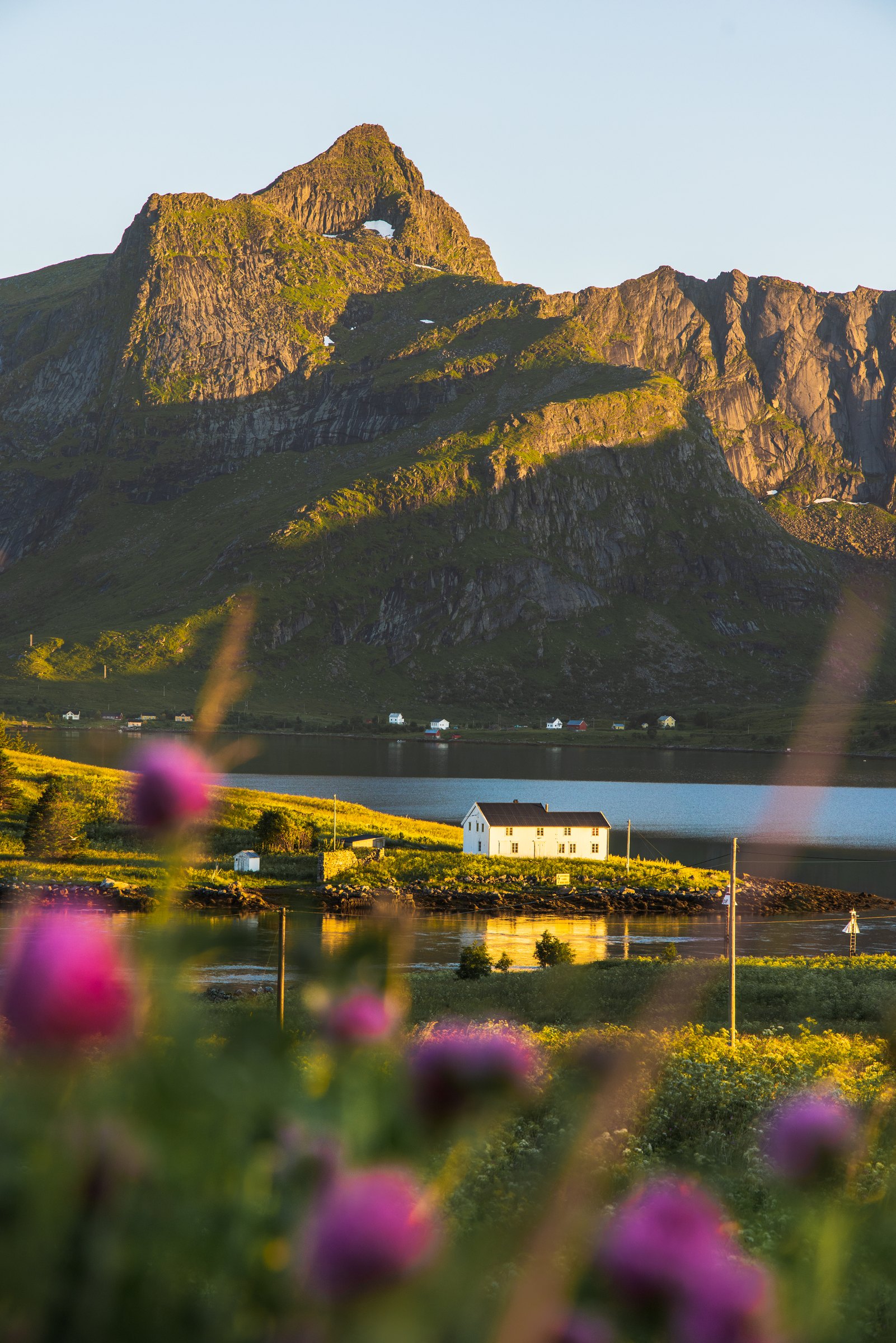 Small house below dramatic green peaks in the Lofoten Islands under the midnight sun