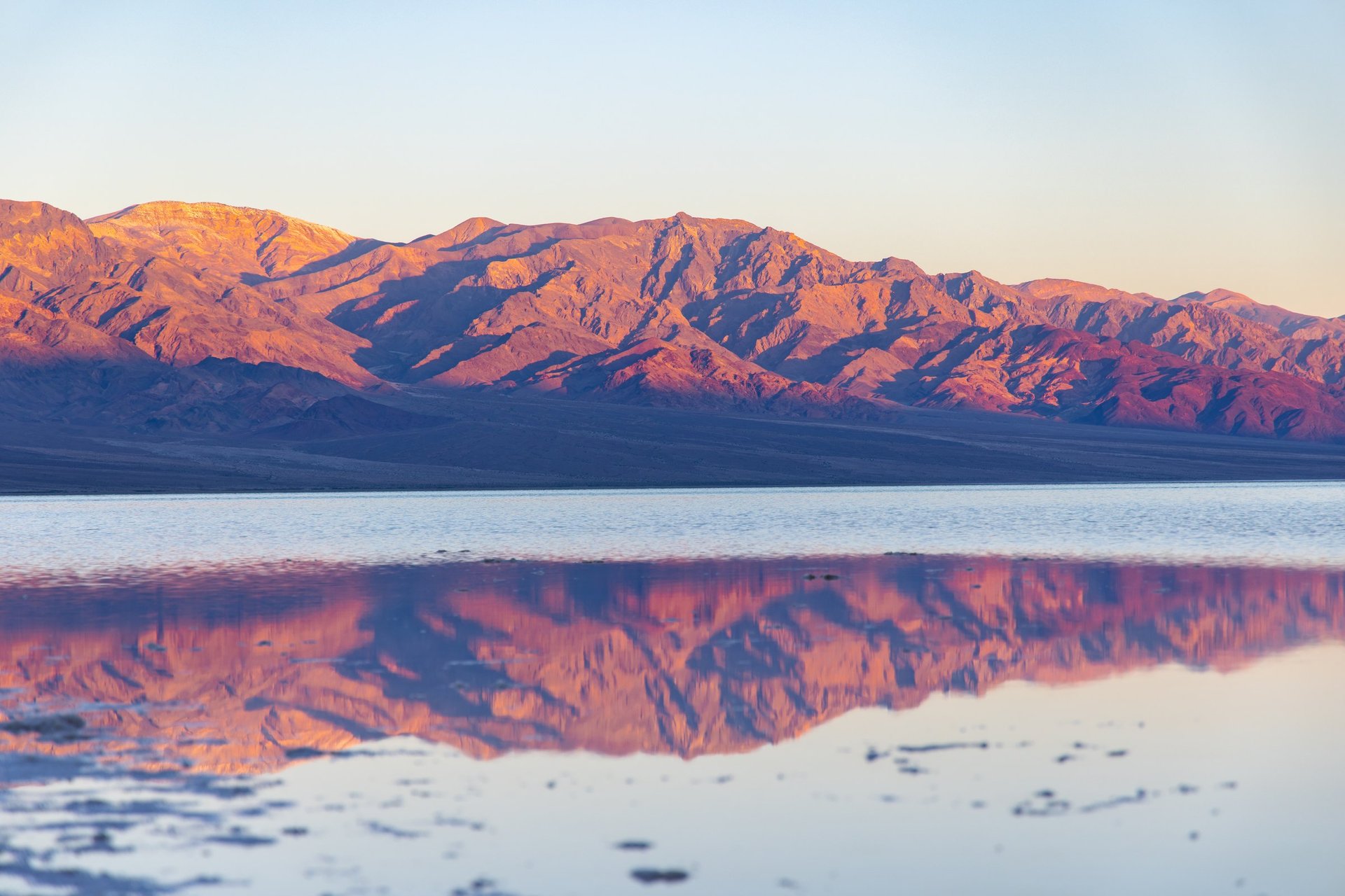 Pink desert mountains at sunrise reflected in a thin layer of rainwater across the salt flats of Badwater Basin, Death Valley