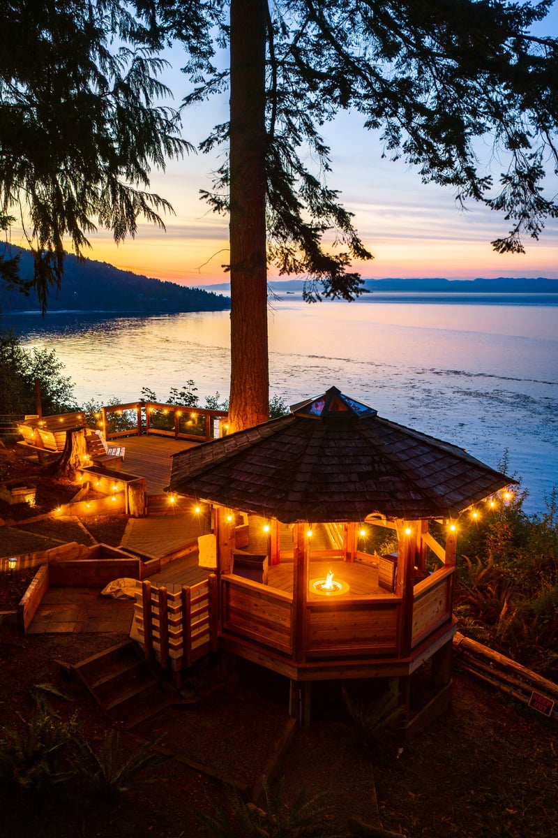 Aerial of a string light gazebo and fire pit on a deck above the water at sunset at a Dreamspace Vacations rental near Port Angeles, Washington