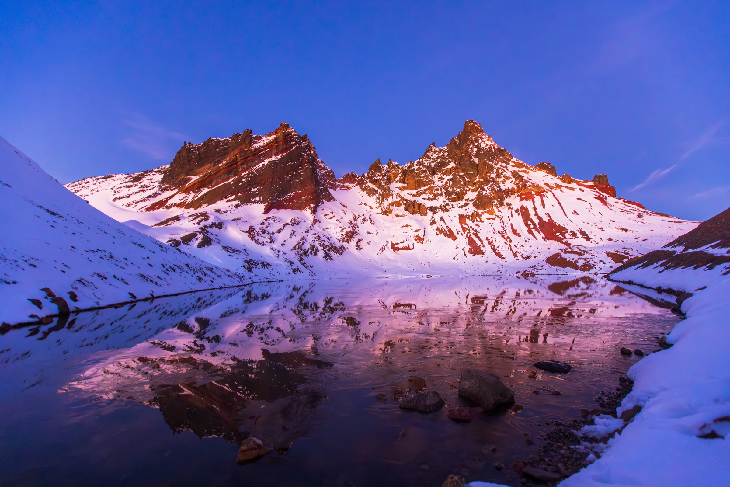 Broken Top's red rock and fresh white snow glowing pink at first light, reflected in a still alpine lake near Bend, Oregon