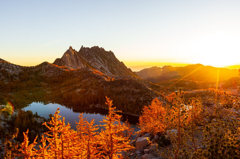 Sunrise over jagged peaks and an alpine lake ringed with golden larches in the Enchantments