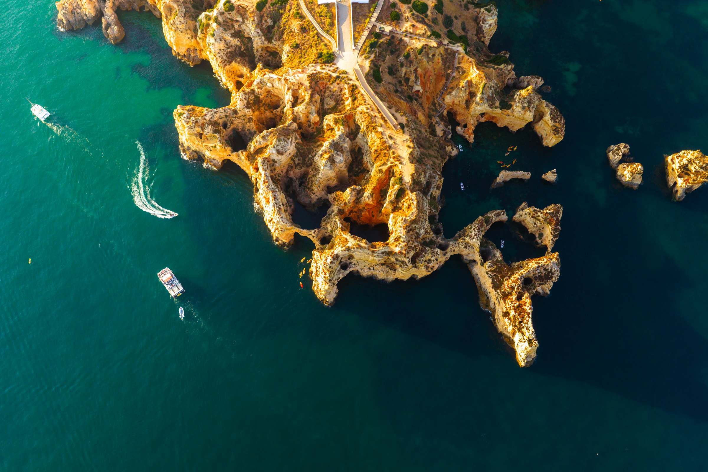 Aerial view of golden sea cliffs and turquoise water with boats near Lagos, Portugal
