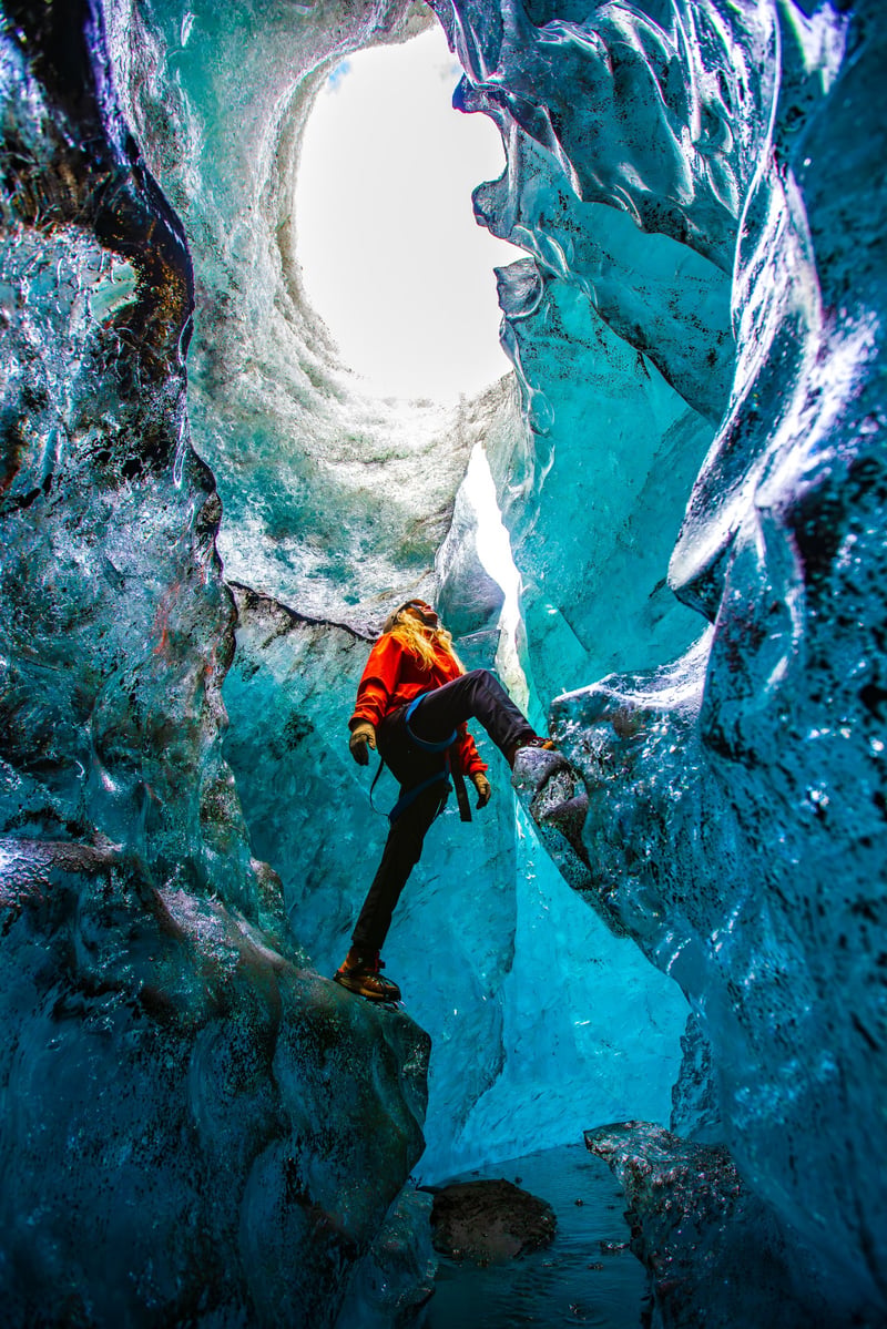 Explorer climbing inside a blue glacier ice cave in Iceland