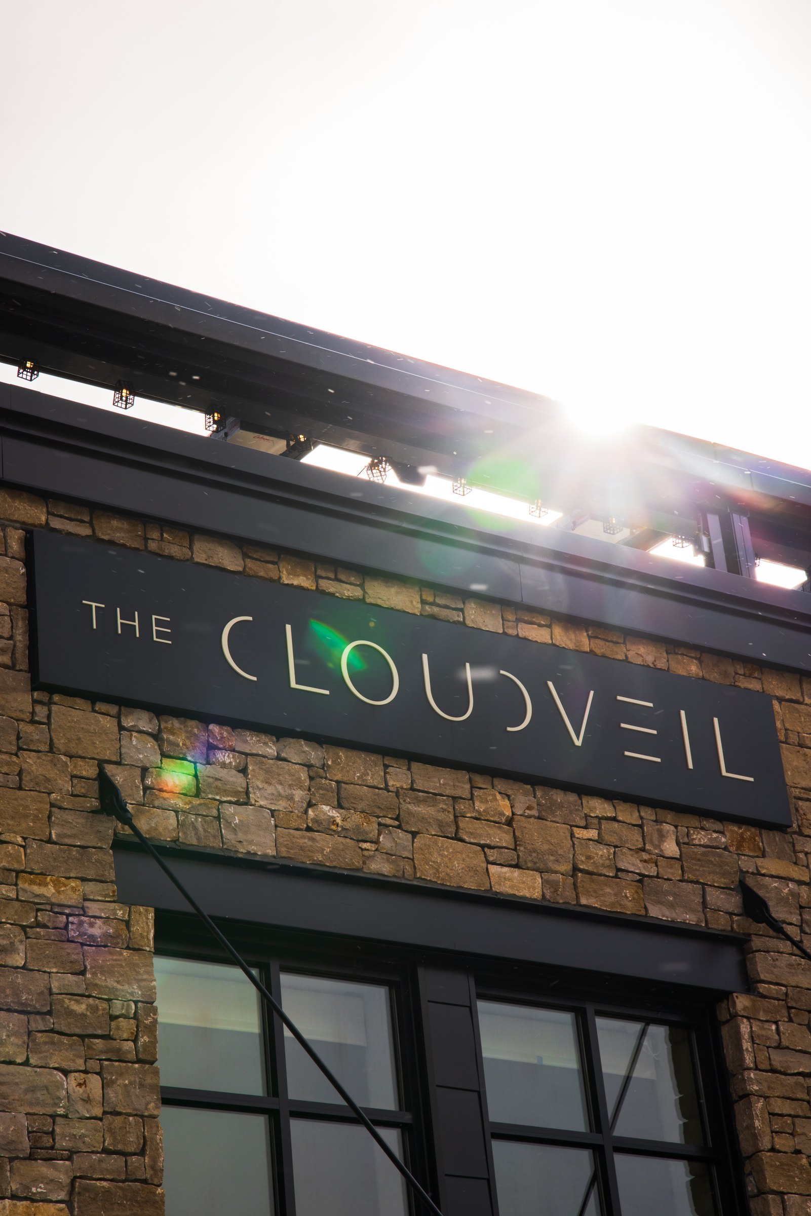 The Cloudveil sign on a stone facade with the sun bursting over the roofline